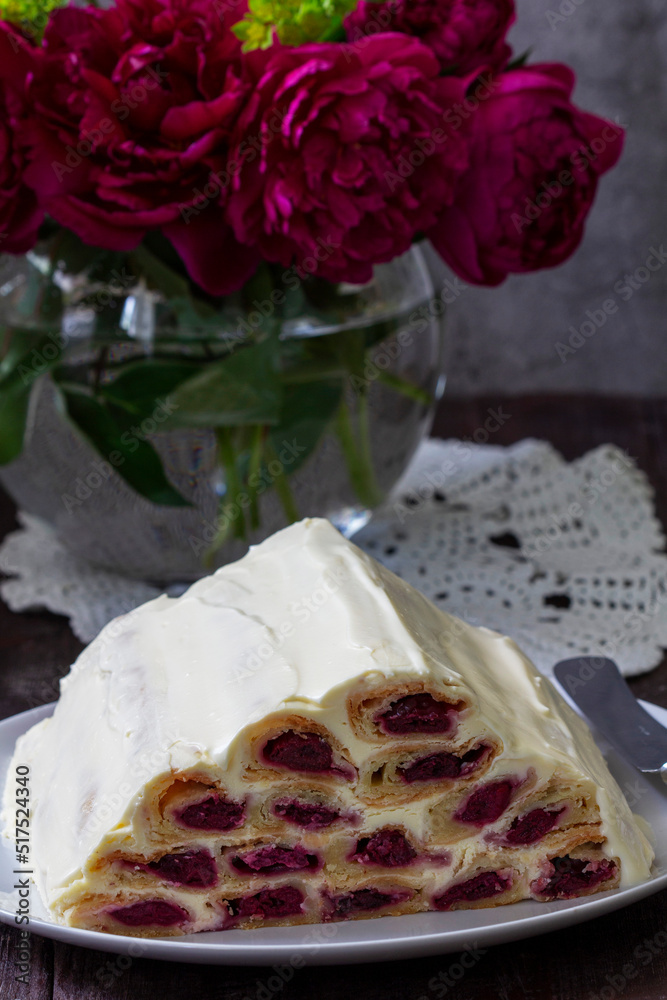 Cake Monastic hut with cherry filling and sour cream, a bouquet of peonies on a wooden table.