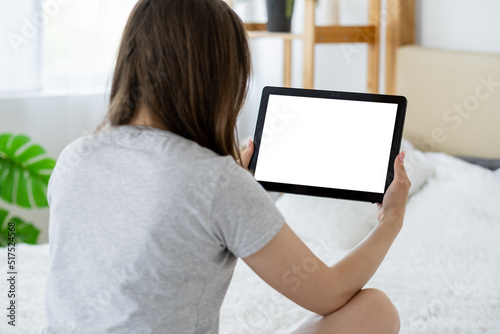 Video conference. Casual woman. Computer mockup. Unrecognizable lady looking tablet computer with blank screen sitting bed in light room interior.