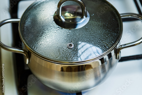 Foto Boiling water in a in a covered stainless saucepan on a gas stove