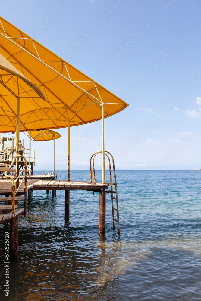 Swimming area or pier on the sea. A large pier with a roof, wooden planks and rusty stairs descending into the water. Bathing and resting place.