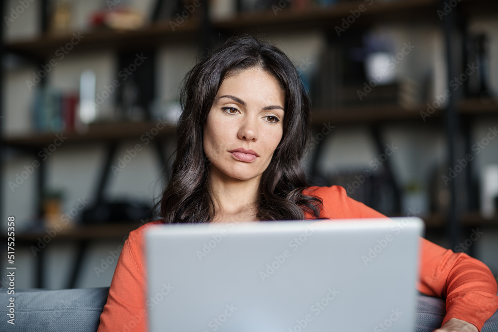 Portrait of focused middle aged woman working on laptop computer sitting on sofa at home. Serious businesswoman working remotely Portrait of focused middle aged woman working on laptop computer sitting on sofa at home. Serious businesswoman working remotely