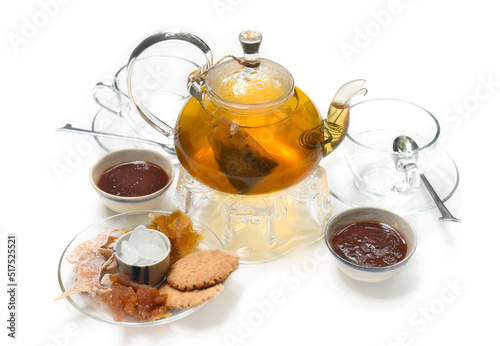 Glass tea pot with cups marmalade and crystalized fruits on white background