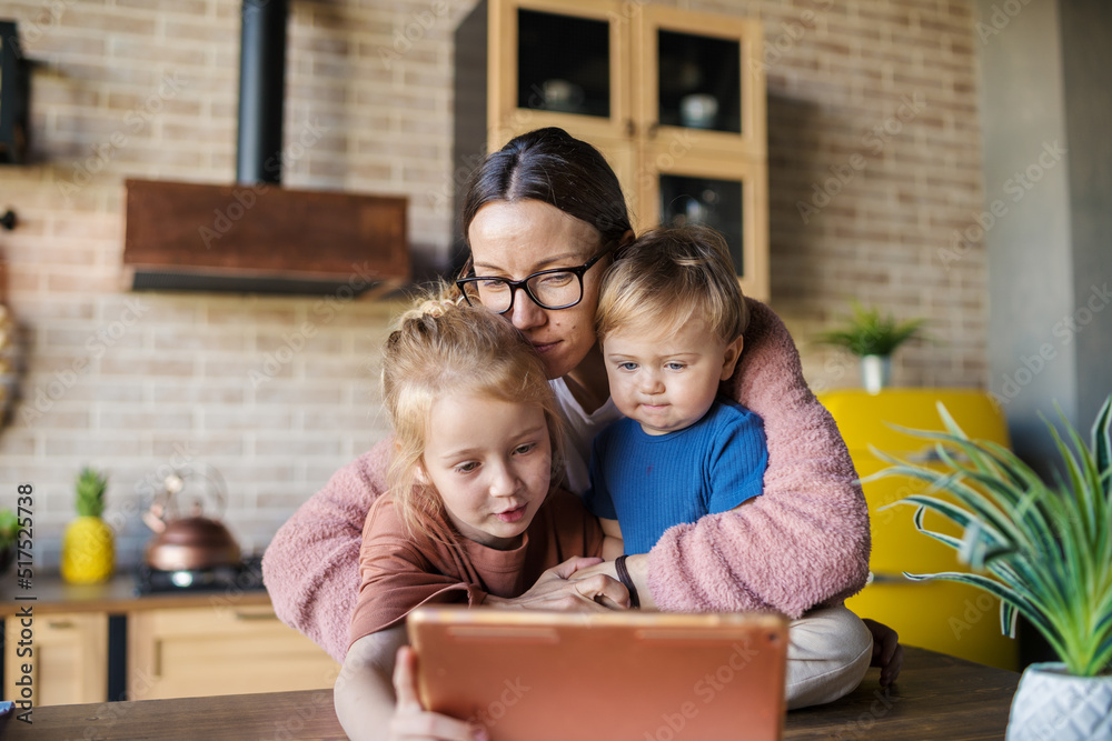 Happy young mother and two kids, little daughter and baby son, watching cartoons on tablet computer. Loving family enjoying time together at home, mom hugging children Happy young mother and two kids, little daughter and baby son, watching cartoons on tablet computer. Loving family enjoying time together at home, mom hugging children