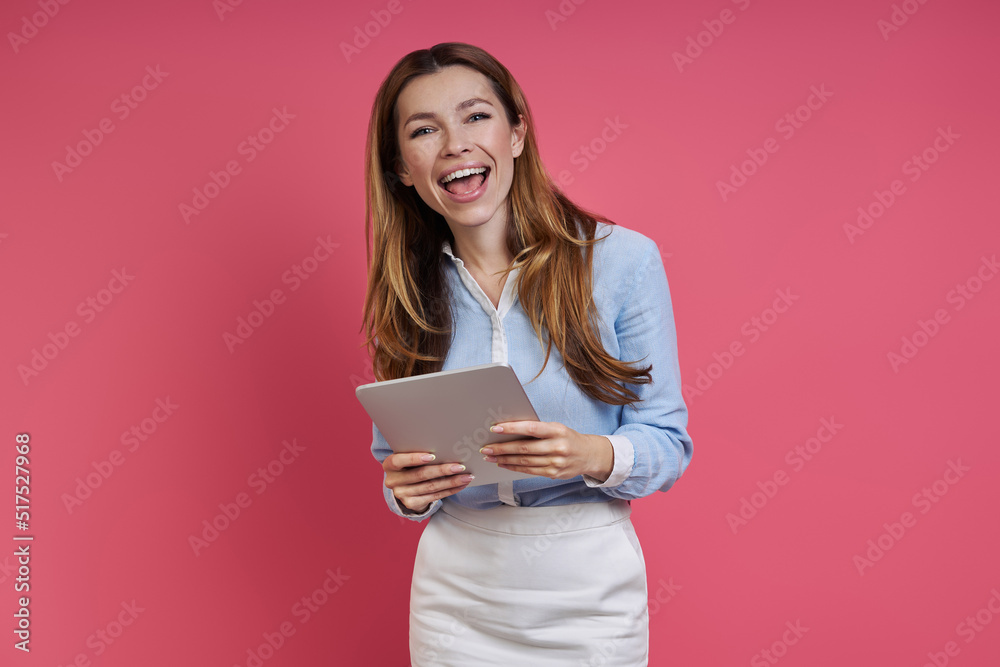 Happy young woman holding digital tablet while standing against colored background Happy young woman holding digital tablet while standing against colored background