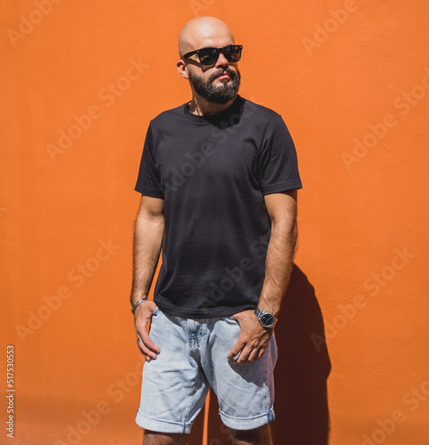 Male model with beard wearing black blank t-shirt on the background of an orange wall