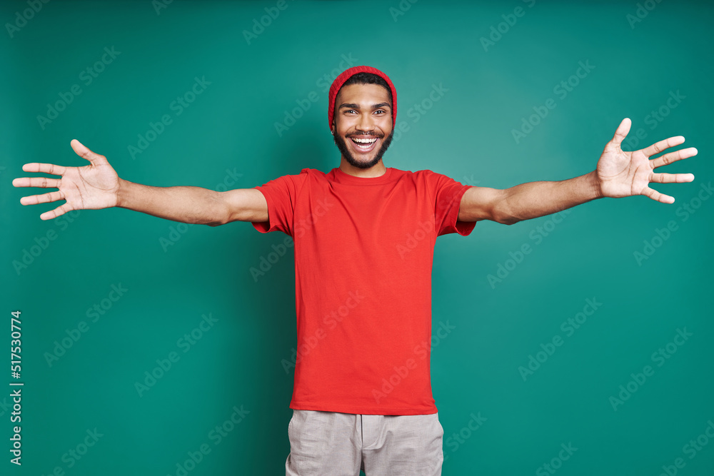 Handsome African man stretching out hands and smiling while standing against green background