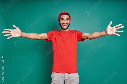 Handsome African man stretching out hands and smiling while standing against green background © gstockstudio