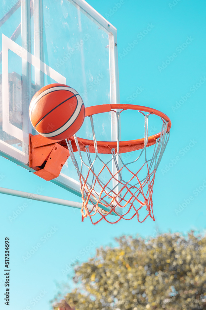 An orange basketball ball in hoop on a blue sky background. Side view