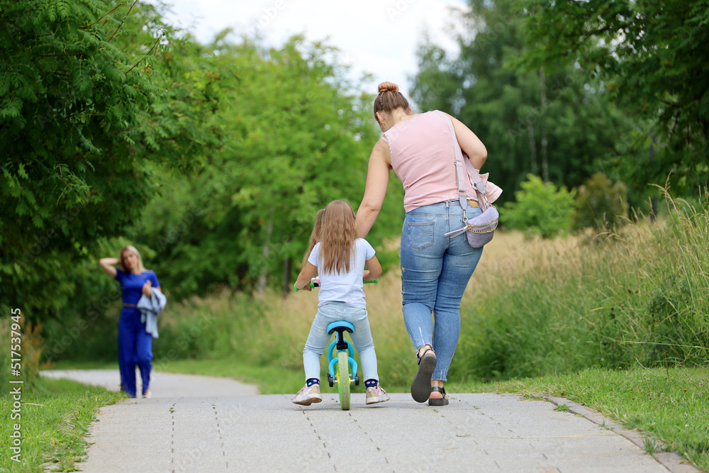 Woman and kid girl with bicycle walking in park. Mother with daughter, family leisure in summer city Woman and kid girl with bicycle walking in park. Mother with daughter, family leisure in summer city