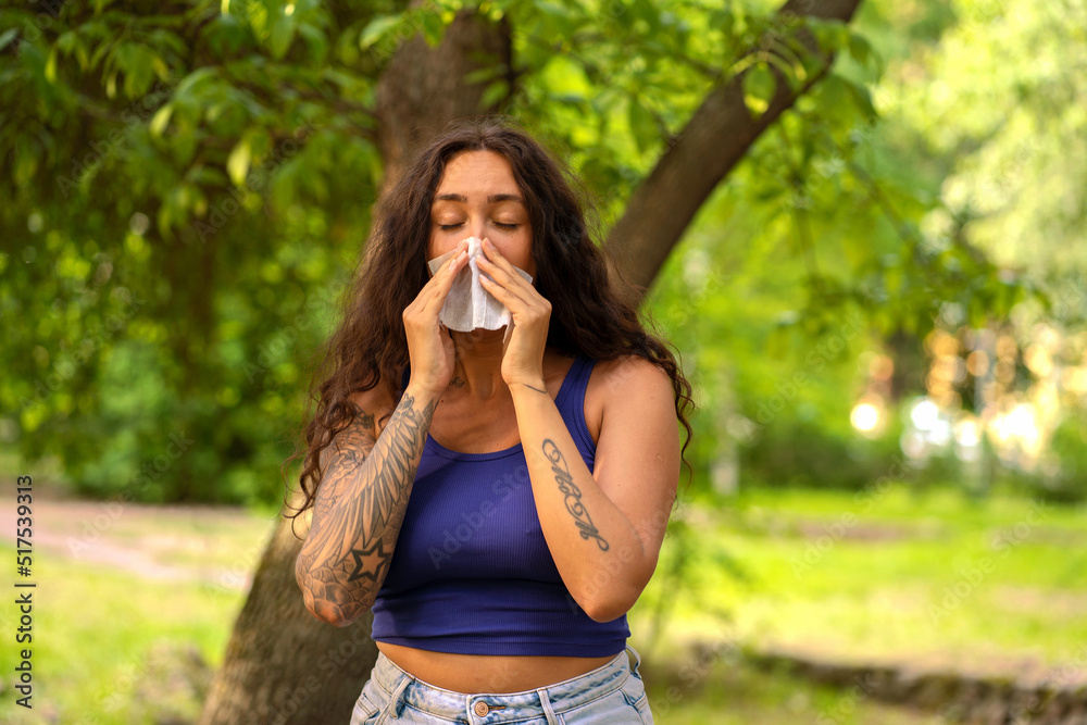A girl stands in a summer park and blows her nose into a handkerchief. Allergy to flowering in a girl. A girl stands in a summer park and blows her nose into a handkerchief. Allergy to flowering in a girl.