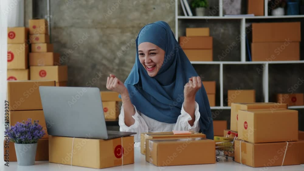 Female Muslim business monger happy and cheerful for successful for receiving orders from customer via laptop with a lot of parcel boxes for shipping. Female Muslim business monger happy and cheerful for successful for receiving orders from customer via laptop with a lot of parcel boxes for shipping.