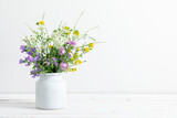 Beautiful bouquet of wild summer flowers in vase against white wall. 