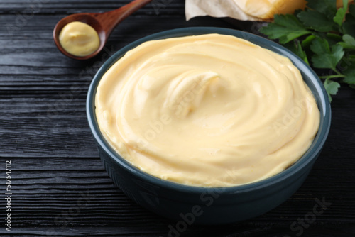 Tasty cheese sauce in bowl on black wooden table, closeup