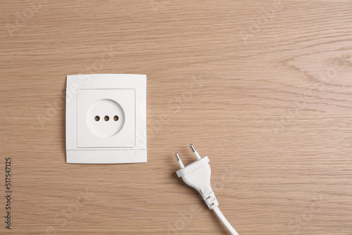 Power socket with plug on wooden table, flat lay. Space for text