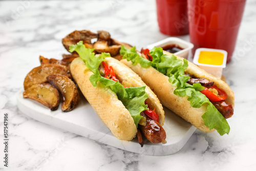 Tasty hot dogs with potato wedges served on white marble table, closeup. Fast food