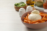 Bowl of delicious pasta with burrata and tomato sauce on white wooden table. Space for text