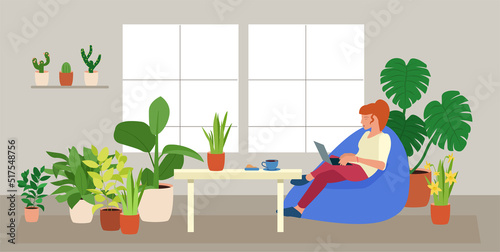 A girl staying home working with laptop sitting in the bean bag chair. A room full of plants. Freelance worker in green interior