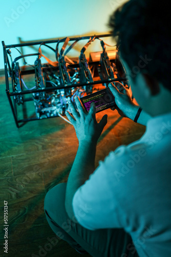 Male programmer adjusting cryptocurrency mining rig to optimal settings with mobile phone