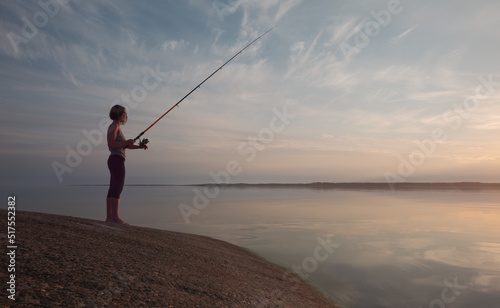 A young girl with a fishing rod in the process of fishing on the shore of the bay