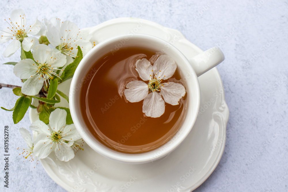 Cup of tea with white flowers on marble table. Minimalist still life in white color. Relaxation, healthy lifestyle, self care concept. Flat lay, top view