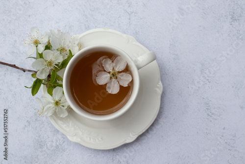 Cup of tea with white flowers on marble table. Minimalist still life in white color. Relaxation, healthy lifestyle, self care concept. Flat lay, top view