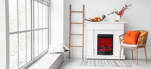 Interior of light room with modern fireplace, armchair and autumn decor