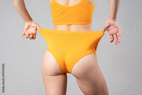 Slim woman in yellow underwear after weight loss on gray background photo