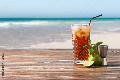 Photography Glass of tasty Cuba Libre cocktail on wooden table at tropical resort