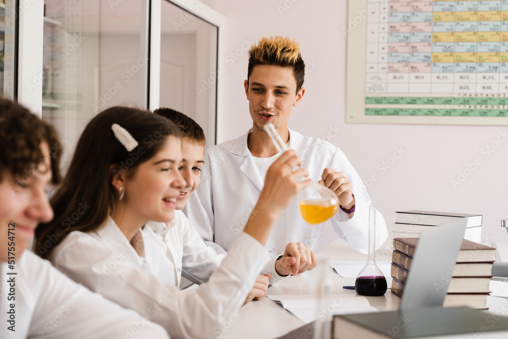 School chemistry teacher shows children flasks with liquids for experiments in the laboratory. Education concept. Group lesson of classmates at chemistry lesson.