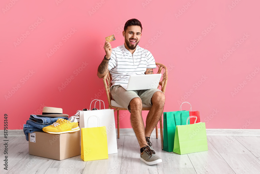 Handsome man with laptop, credit card and shopping bags on pink background Handsome man with laptop, credit card and shopping bags on pink background