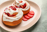 Plate with strawberry cinnamon rolls and cream on color background