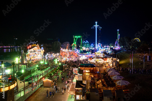 Aerial top view of amusement park, carnival or festival called Größte Kirmes am Rhein, with crowd of visitors during night time.