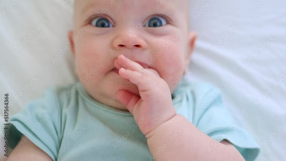 funny infant face portrait, blue eyes happy smiling baby child 3 months on white sheets. caucasian kid close-up portrait. happy little baby lying in bed looking into camera making funny grimaces. funny infant face portrait, blue eyes happy smiling baby child 3 months on white sheets. caucasian kid close-up portrait. happy little baby lying in bed looking into camera making funny grimaces.