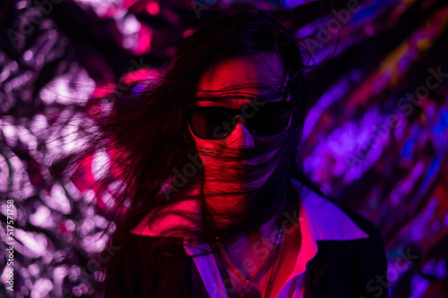 Portrait of a transgender model in sunglasses in a studio with neon lighting.