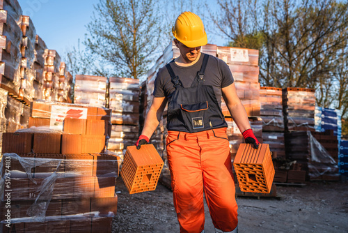 One man construction worker taking and carry or hold clay orange hollow blocks ar warehouse or construction site in sunny summer day copy space