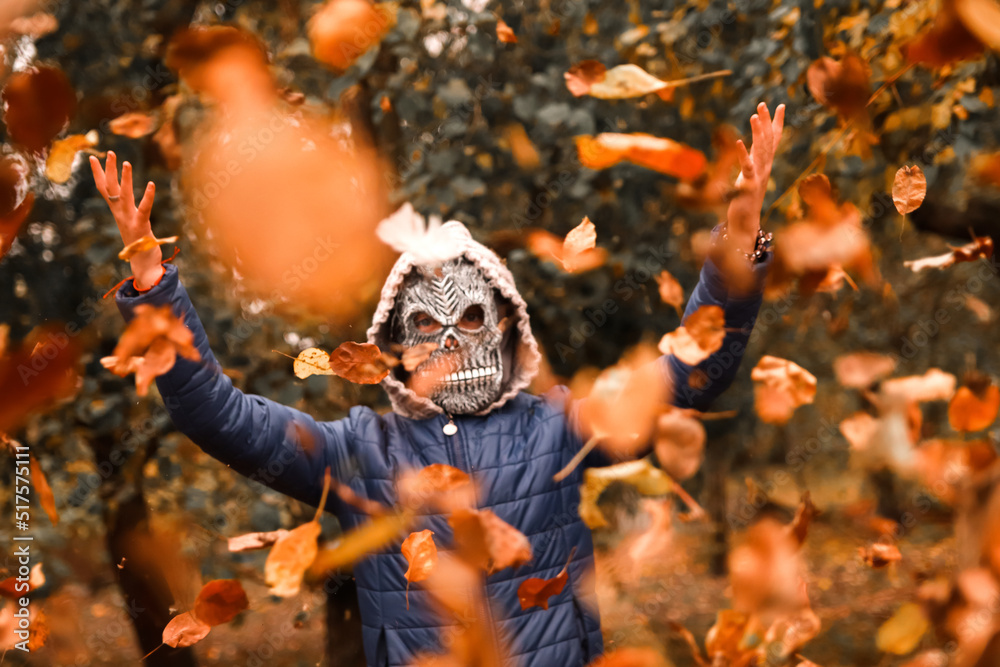 Defocus Halloween people. Person in grim reaper mask raising hand and throwing leaves. Many flying orange, yellow, green dry leaves. Creepy people Fall park. Demon costume. Vintage tone. Out of focus Defocus Halloween people. Person in grim reaper mask raising hand and throwing leaves. Many flying orange, yellow, green dry leaves. Creepy people Fall park. Demon costume. Vintage tone. Out of focus