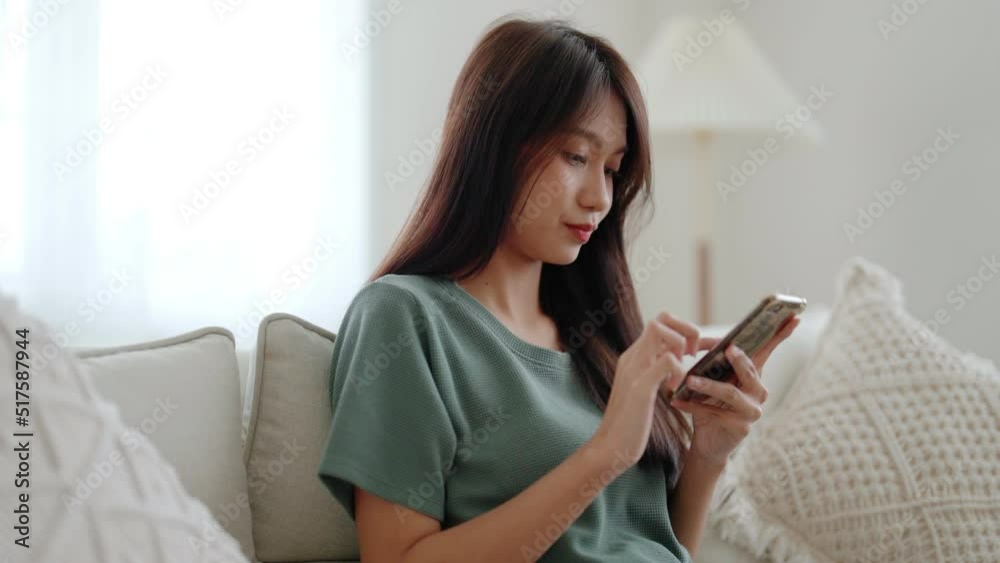 Happy young asian woman relax on comfortable couch at home texting messaging on smartphone, smiling girl use cellphone chatting, browse wireless internet on gadget, shopping online from home Happy young asian woman relax on comfortable couch at home texting messaging on smartphone, smiling girl use cellphone chatting, browse wireless internet on gadget, shopping online from home