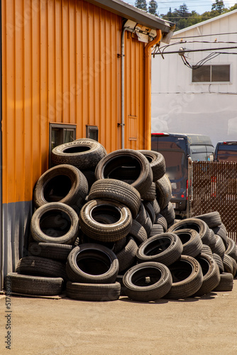Stacked tires await disposal outside of a tire repair shop.
