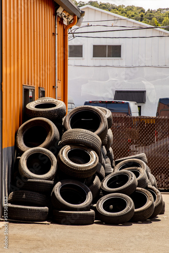 Stacked tires await disposal outside of a tire repair shop.