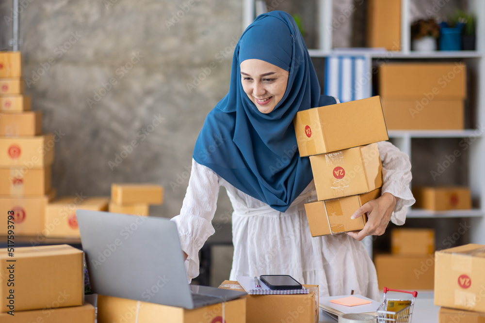 Muslim young Asian woman working at home doing sme ecommerce online small business entrepreneur checking postal parcels to delivery to online customers, startup Muslim Sme business concept. Muslim young Asian woman working at home doing sme ecommerce online small business entrepreneur checking postal parcels to delivery to online customers, startup Muslim Sme business concept.