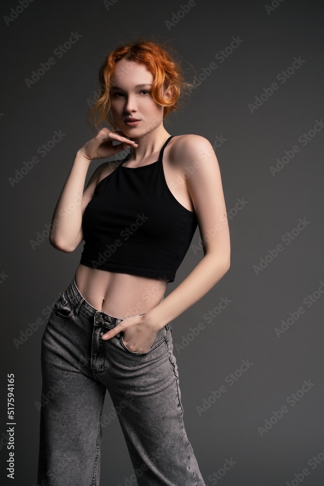 Confident young woman standing in gray studio with hand on waist Confident young woman standing in gray studio with hand on waist