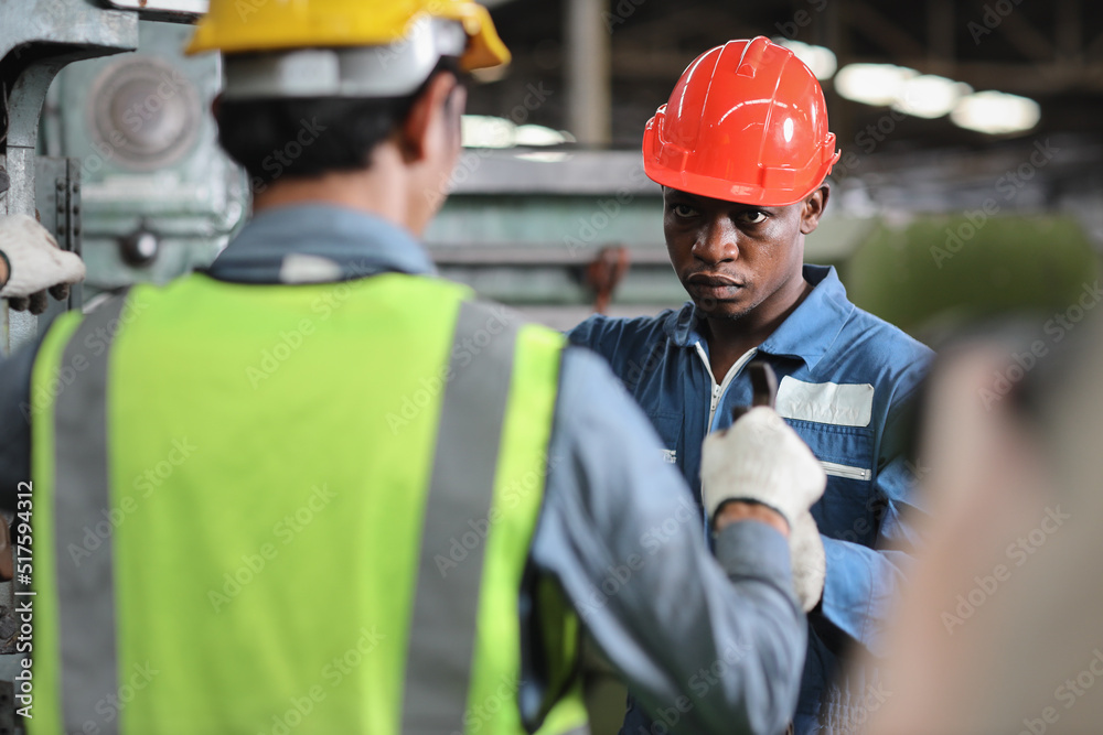 Technician engineer in protective uniform with hardhat standing and teaching apprentices or colleague worker to use computerized machine control at heavy industry manufacturing factory Technician engineer in protective uniform with hardhat standing and teaching apprentices or colleague worker to use computerized machine control at heavy industry manufacturing factory