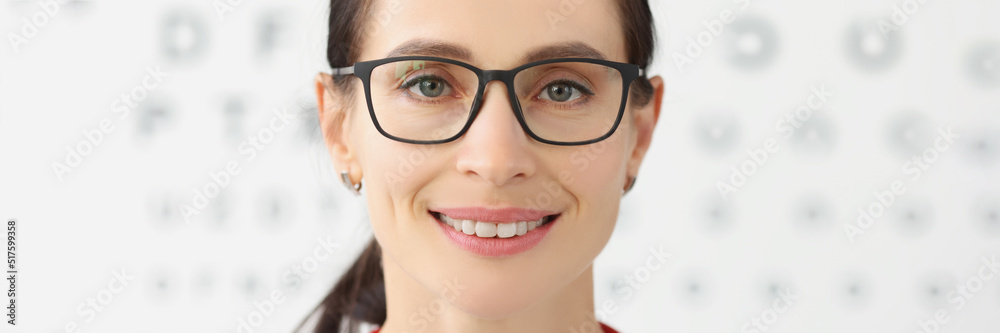 Smiling female eye doctor with eye test chart on background, female optician in glasses Smiling female eye doctor with eye test chart on background, female optician in glasses