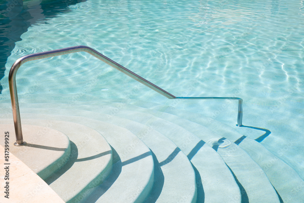 Steps going into aqua blue swimming pool with metal hand rail 
