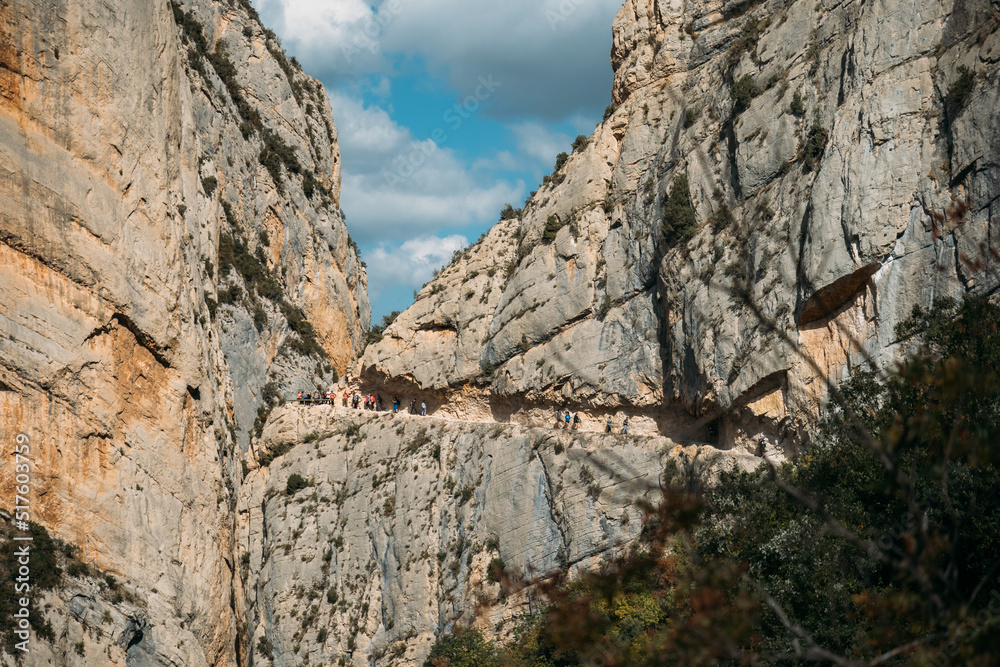 Spectacular cliff with a walkway inside the rock with people doing hiking trips. Congost de Mont Rebei, Catalonia, Spain.