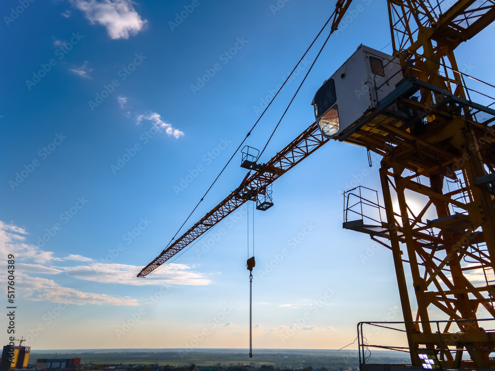 Construction crane on the background of a clear day sky aerial view. Flyby of a construction crane on a quadrocopter against the background of an epic blue sky with the sun, close-up