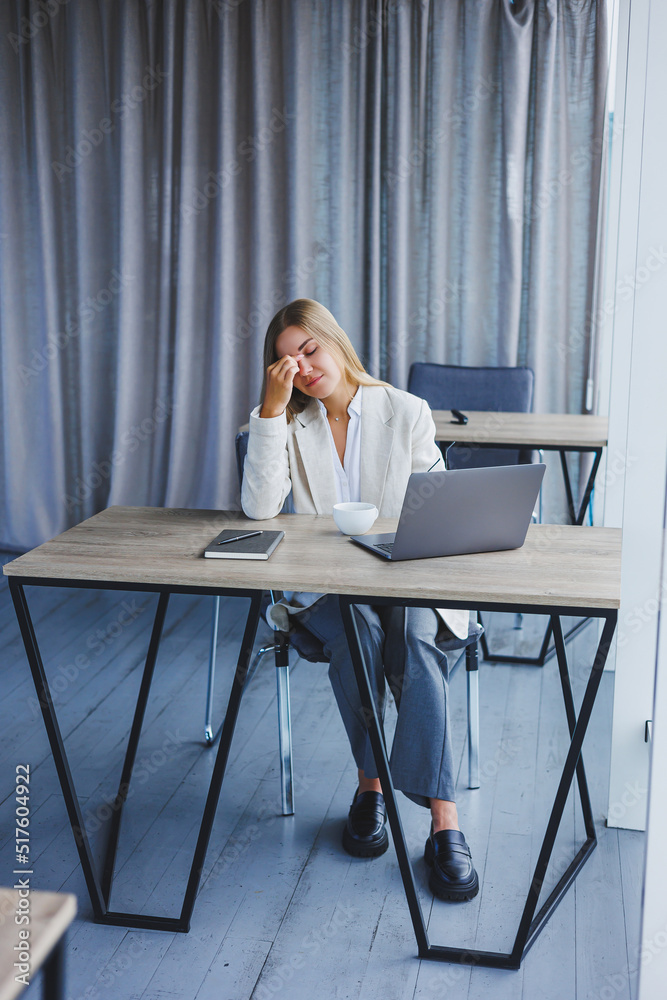 Manager focused woman in casual wear and eyeglasses typing on netbook while working on new project sitting at table in modern workspace Manager focused woman in casual wear and eyeglasses typing on netbook while working on new project sitting at table in modern workspace