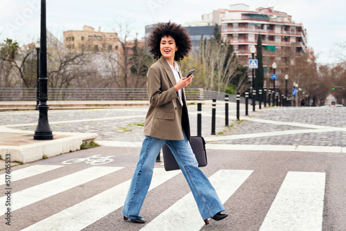 smiling young business woman walking on a crosswalk using her smart phone, concept of communication and urban lifestyle photo