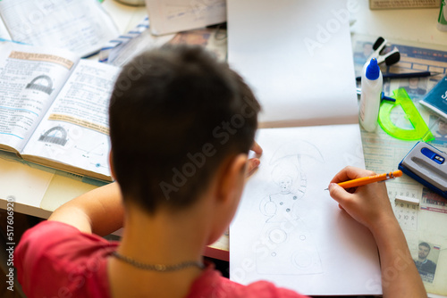 The boy at the table draws, does homework, is engaged in creativity. A man holds his head with his hand. a table stands by the window