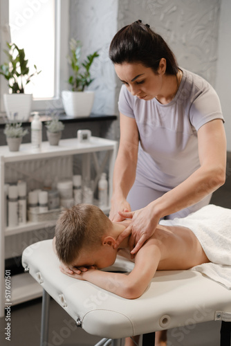 masseur gives the child a back massage. Kids massage concept. massage therapist giving 7 year old boy shoulder massage. Physical therapy
